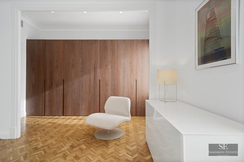 Minimalist dressing area with floor-to-ceiling wood wardrobes, herringbone parquet, and a white designer chair.