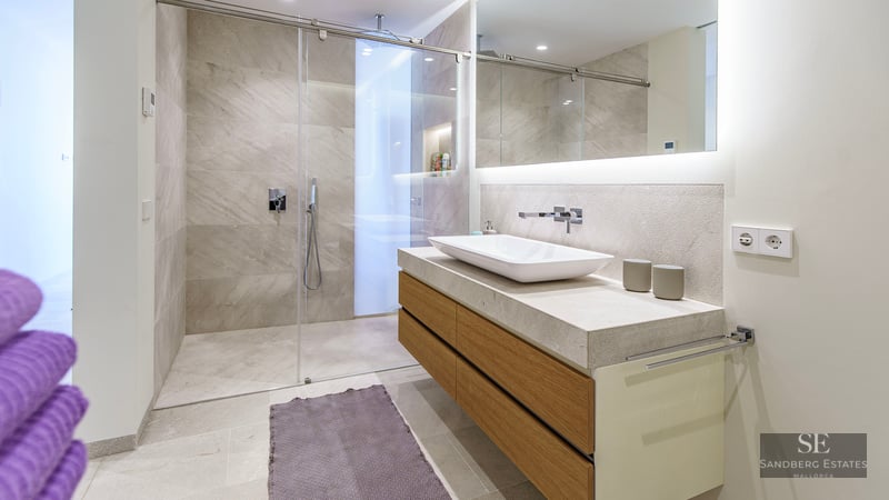 Salle de bain moderne avec douche en verre, meuble en bois avec vasque blanche et grand miroir rétroéclairé.