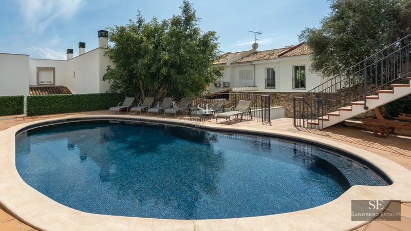 Aerial view of a modern villa featuring a swimming pool, lush garden, and sleek architectural design. Abundant natural lighting.