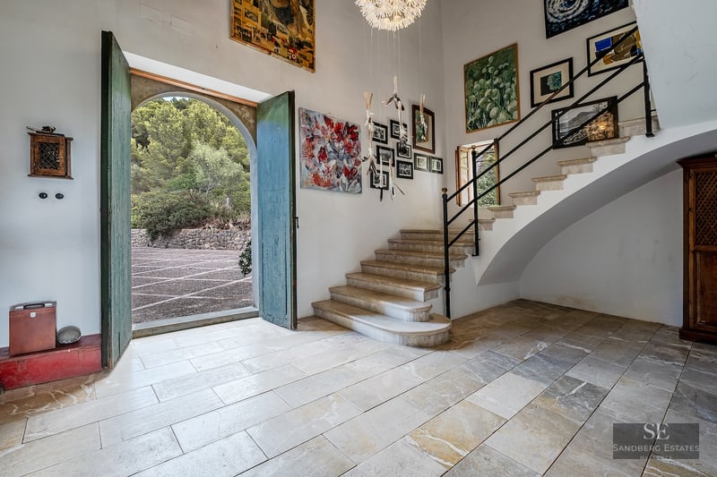 Grand entrance hall with stone floors, high ceilings, a stone staircase, and large green arched doors open to the outside.