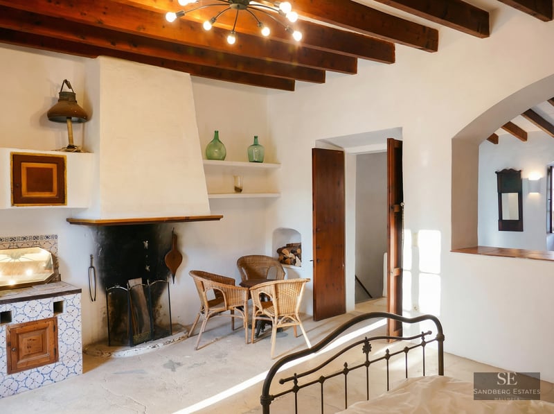 Master bedroom featuring exposed wood beams, a large white fireplace, and rustic wicker seating.