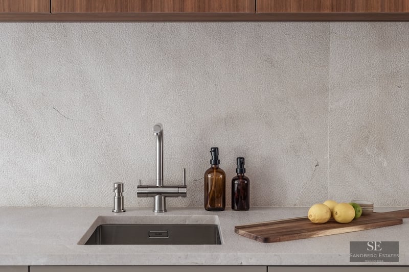 Close-up of a kitchen sink with a stainless steel faucet, stone countertop, and wooden cutting board.
