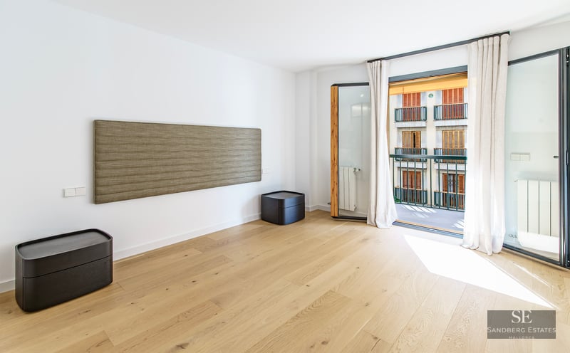 Chambre moderne avec parquet en bois clair, tête de lit murale texturée et balcon baigné de lumière naturelle.