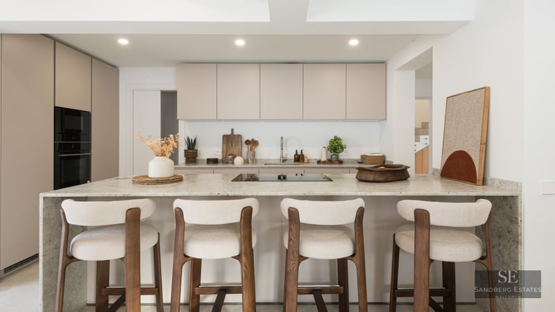 Modern kitchen with beige cabinets, a large stone island, and four wood and fabric bar stools.