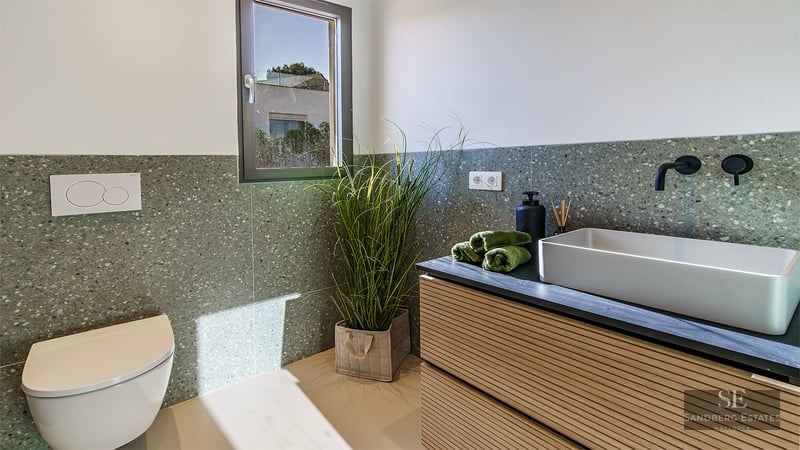 Minimalist bathroom featuring a vessel sink, black faucet, wall-hung toilet, and green terrazzo walls.