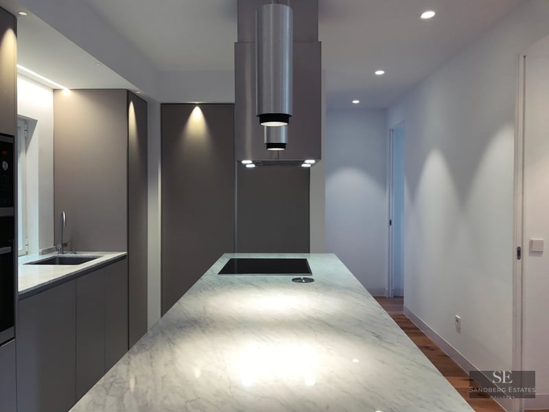 Modern kitchen featuring a large white marble island, matte grey cabinetry, and a sleek cylindrical extractor hood.