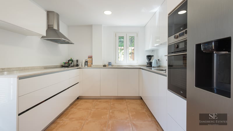 Modern U-shaped kitchen featuring glossy white cabinets, terracotta tile flooring, and stainless steel appliances.