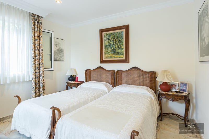 Bedroom featuring two twin beds with wicker headboards, marble flooring, and framed artwork.