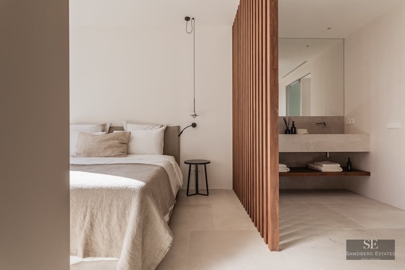 Minimalist beige bedroom separated from a stone vanity by vertical wooden slats.