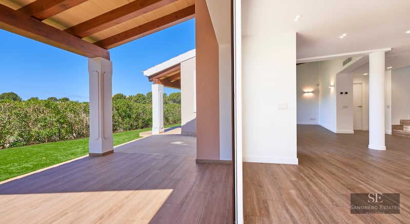 View of a modern terrace with wooden beams and tiled floor connecting to a green lawn under a clear blue sky.