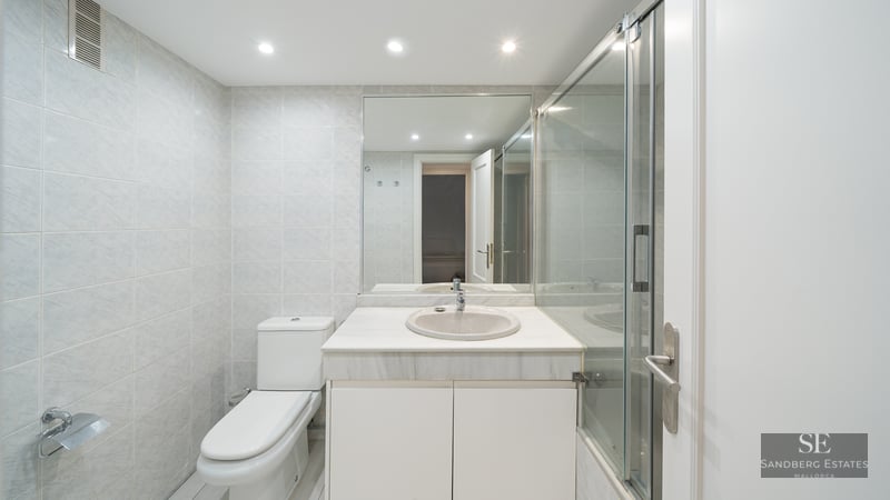 Bright bathroom featuring a white marble vanity, glass shower enclosure, and light grey wall tiles.