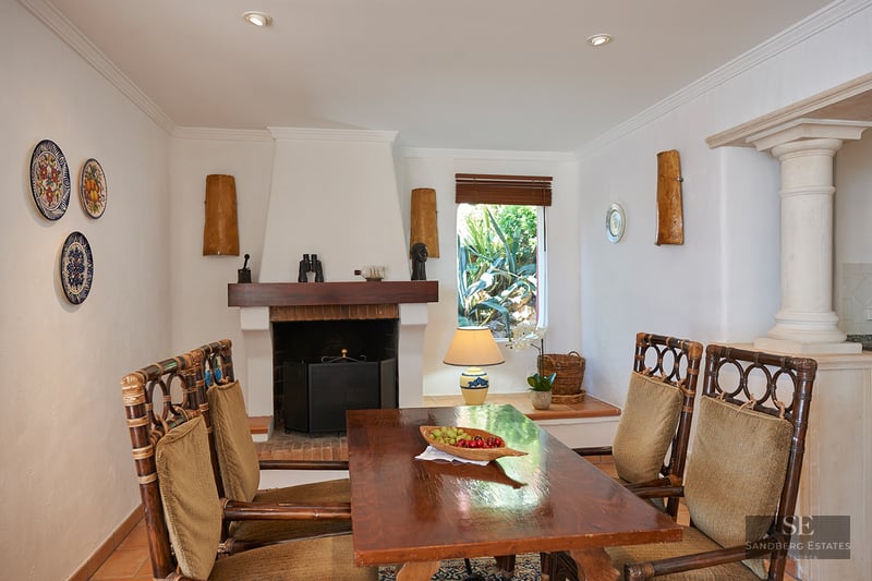 A dining room featuring a wooden table, bamboo chairs, a white fireplace, and decorative wall plates.