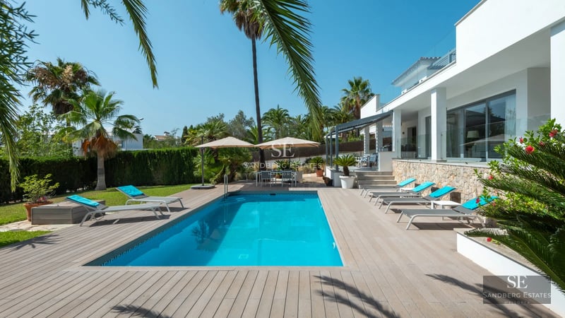 Wide view of bright living room with infinity pool and modern furniture. Large windows and lush garden.