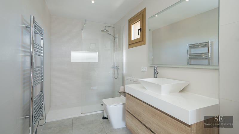 Modern bathroom featuring a walk-in glass shower, wooden vanity with square sink, and chrome heated towel rail.