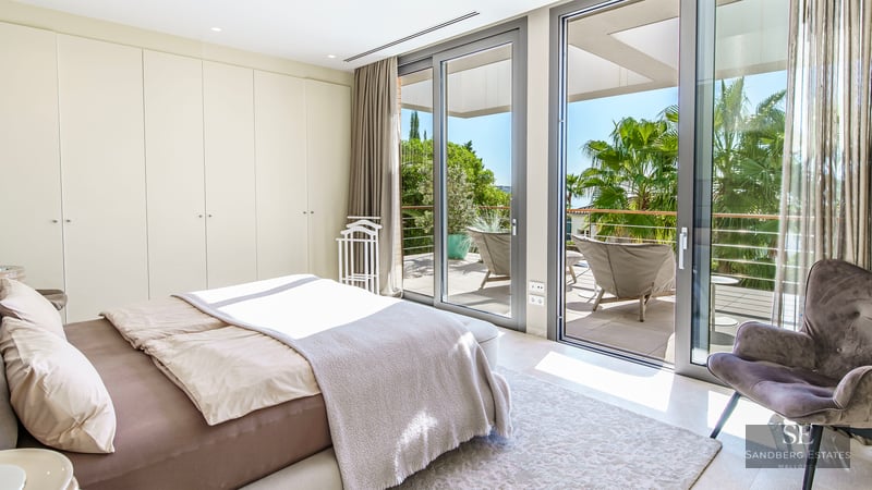 Chambre moderne avec baies vitrées donnant sur une terrasse ensoleillée et des palmiers.