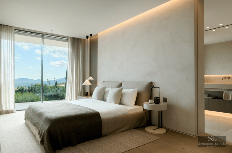 Minimalist master bedroom featuring floor-to-ceiling windows with mountain views and an open ensuite bathroom.