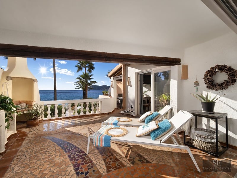 Sunlit terrace with mosaic floors, white loungers, and a stunning view of the blue ocean and palm trees.