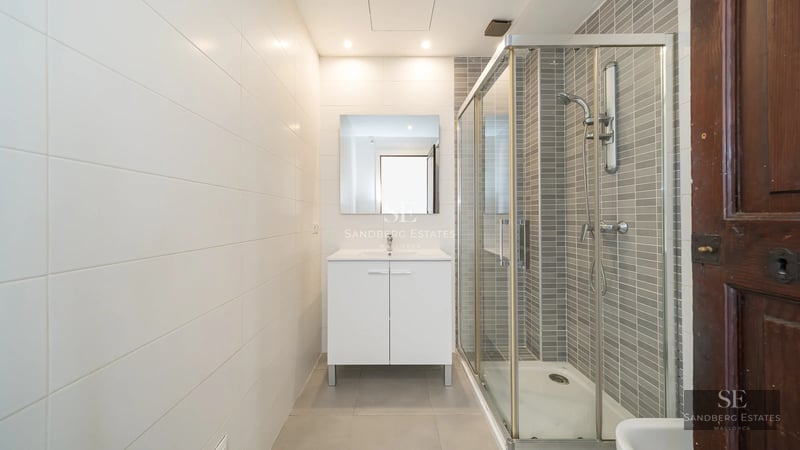 Spacious balcony with sea view. Glass railing, tiled floor, modern outdoor furniture. Blue sky, calm sea.