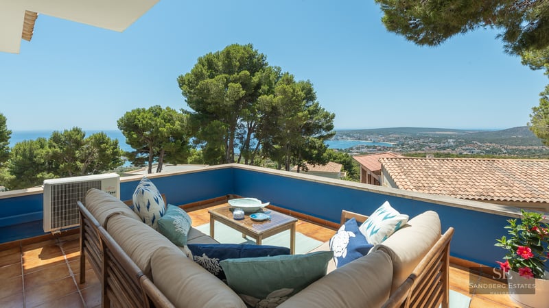 Outdoor terrace with L-shaped sofa, blue walls, and panoramic views of the Mediterranean coastline.