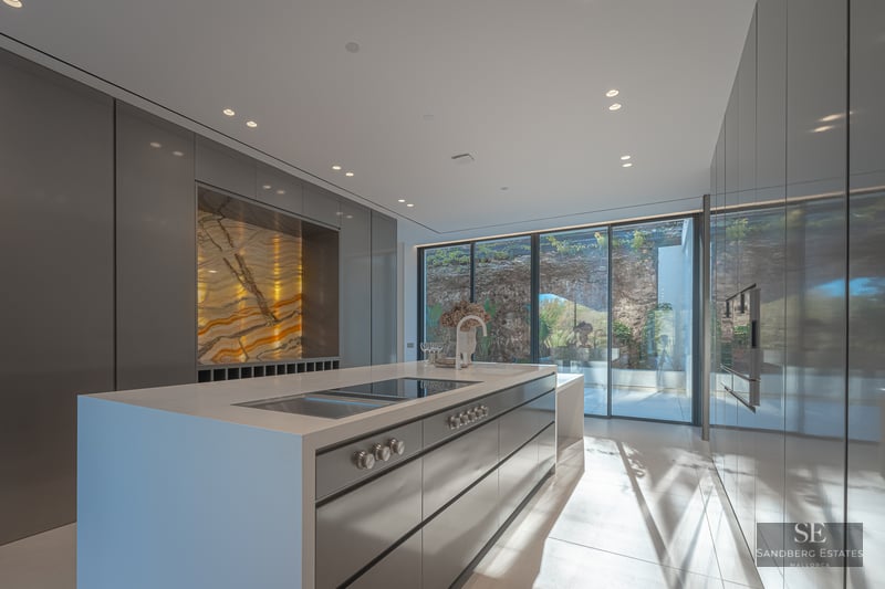 Modern minimalist kitchen with large island, sleek grey cabinetry, and a stunning backlit golden marble feature wall.