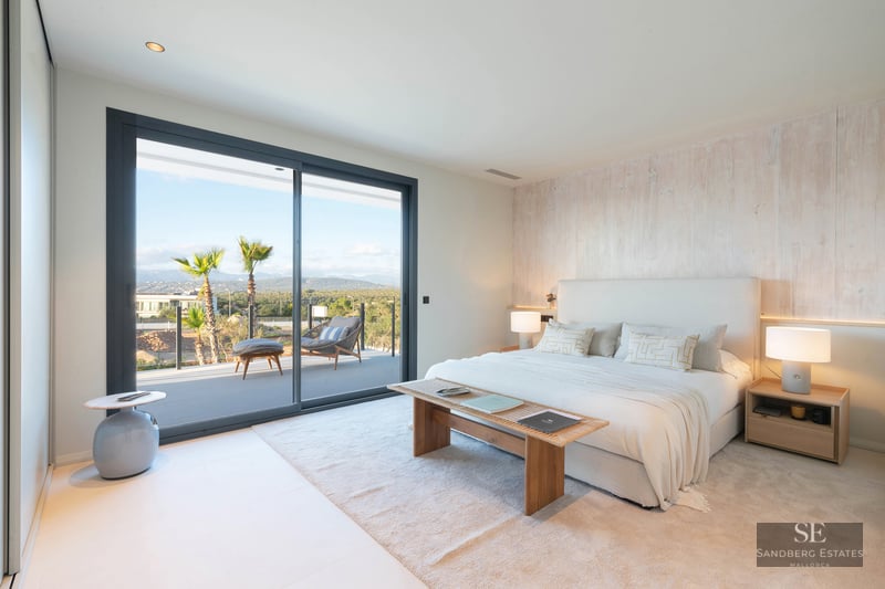 Luxury bedroom with white bed, wood accent wall, and glass door opening to a terrace with mountain views.