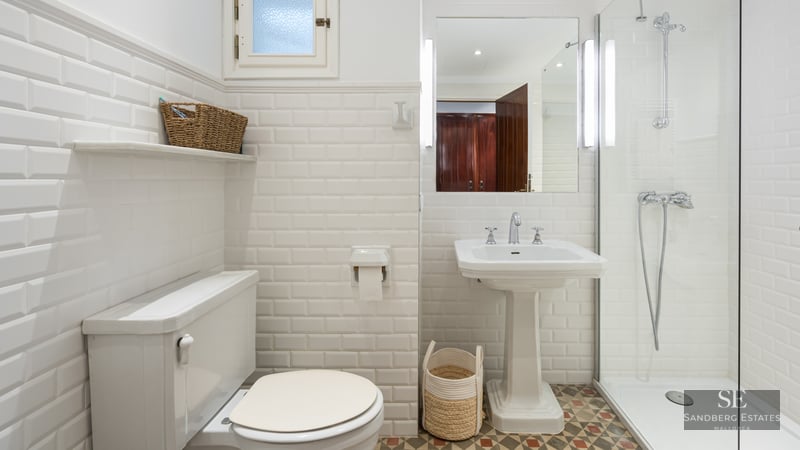 Bright bathroom with white subway tiles, pedestal sink, glass shower, and patterned floor tiles.