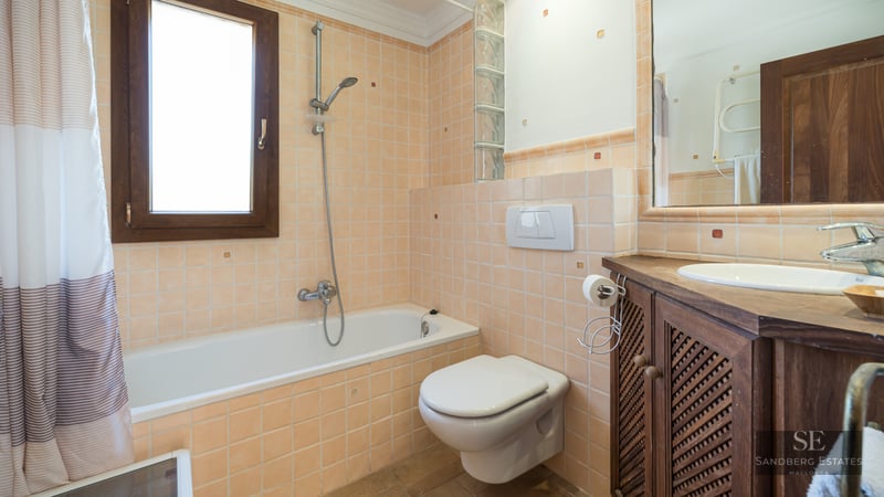Bathroom featuring peach tiling, a bathtub, wall-hung toilet, and a dark wood vanity unit.