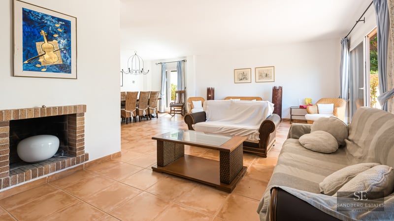 Large living room with terracotta tile floors, wicker furniture, a brick fireplace, and an adjacent dining area.