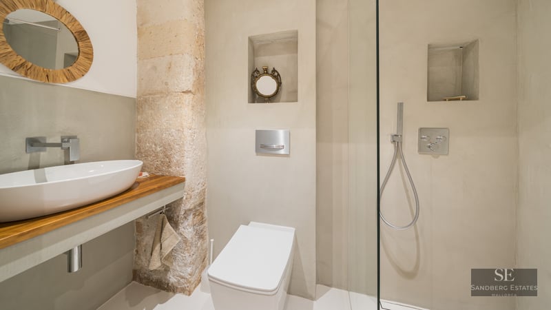 Modern bathroom featuring a white vessel sink, glass walk-in shower, natural stone pillar, and microcement walls.
