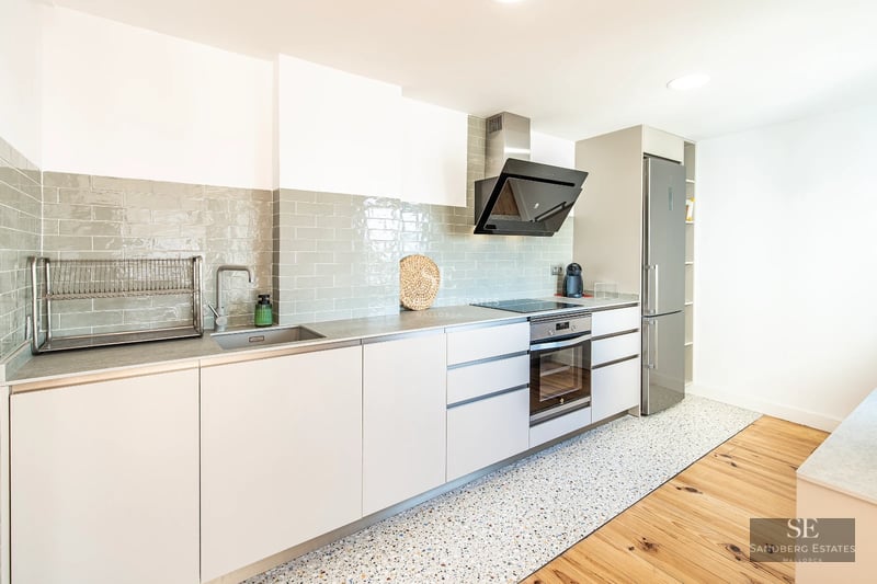 Exterior view of a modern villa with infinity pool, large terrace, and lush garden under a sunny sky.