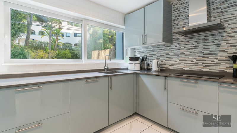 Cuisine moderne avec meubles bleu clair, plans de travail gris, grande fenêtre et crédence en mosaïque.