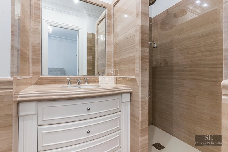 Spacious living room with floor-to-ceiling windows, natural light, light wood floors, and modern furniture. View of the garden with pool.