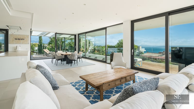 Spacious living room with white sofas, wooden coffee table, and large glass doors opening to a sea-view terrace.