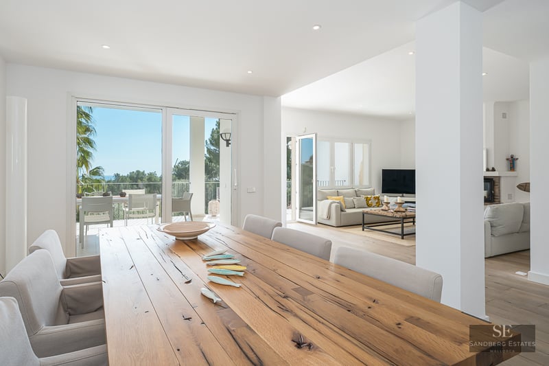Grande table à manger en bois rustique dans une pièce moderne et lumineuse avec accès à une terrasse panoramique.