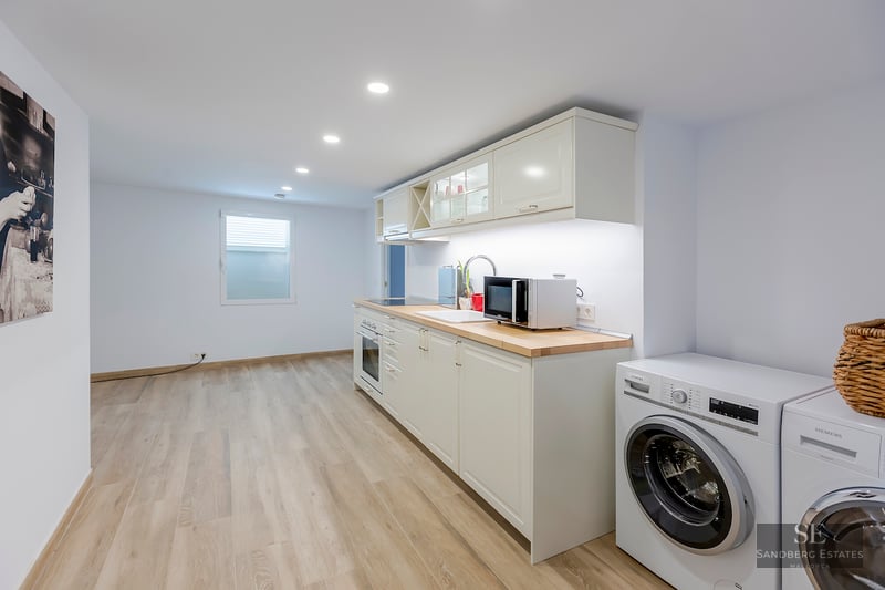 Bright modern kitchen with white cabinets, light wood countertops, and integrated washing machine and dryer.