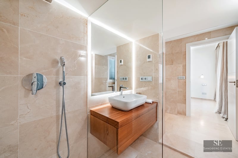 Modern bathroom featuring beige marble walls, a glass walk-in shower, and a floating wood vanity with a white vessel sink.