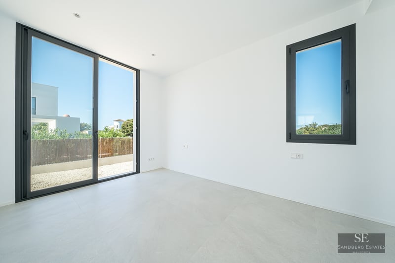 Empty modern room with white walls, grey tile flooring, and a large sliding glass door leading to a patio.