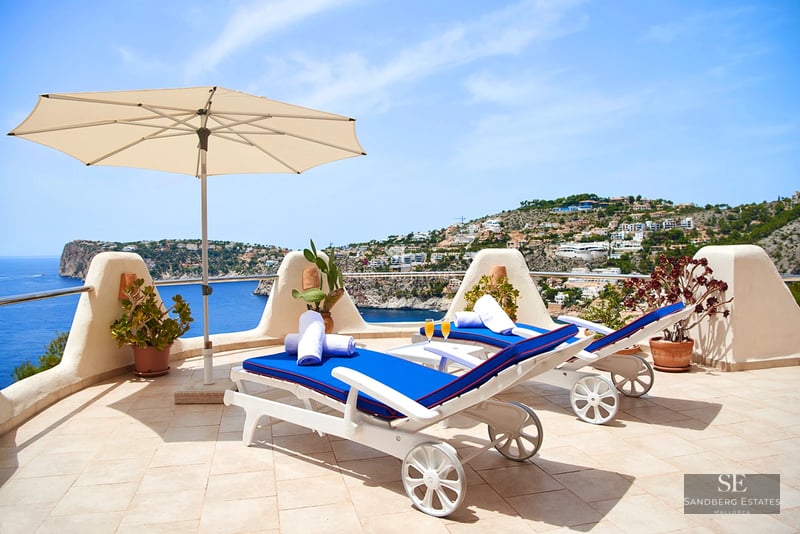 Spacious terrace with pool, sun loungers, and panoramic sea views. Modern design with glass railing and wooden flooring.