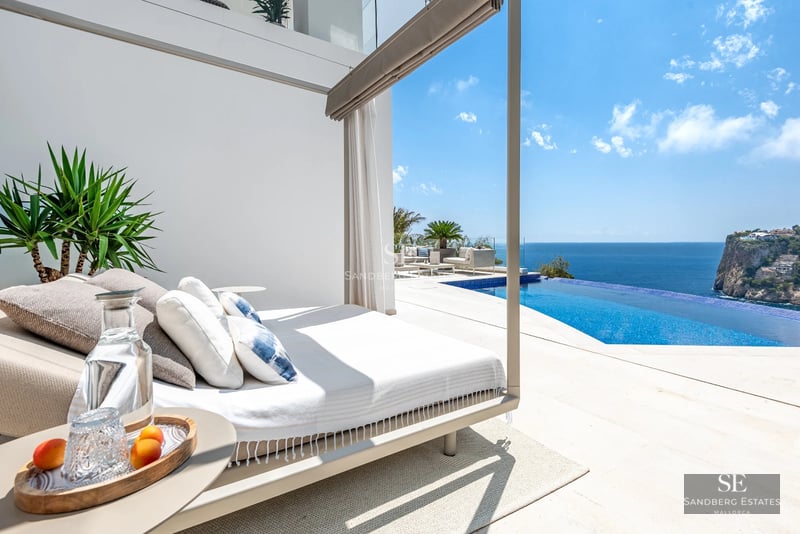 Balcony with panoramic sea views. Modern design, glass railing, wooden flooring, stylish outdoor furniture.