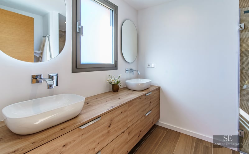 Modern bathroom featuring a long wooden vanity with two white vessel sinks and backlit circular mirrors.