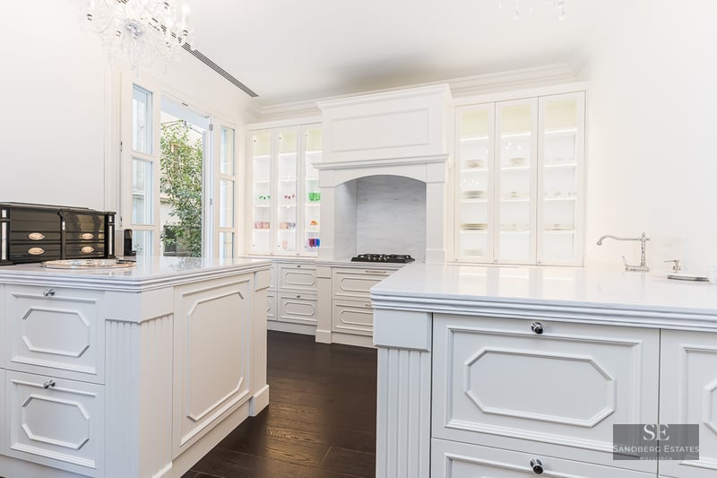 Elegant kitchen featuring white cabinetry, marble countertops, a central island, and a crystal chandelier.