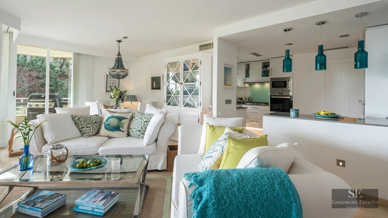 View of an infinity pool with lounge chairs and a modern house featuring large windows and a lush garden in the background.