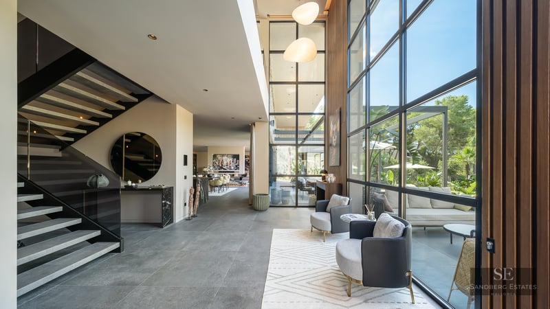 Grand modern living area featuring a minimalist staircase, floor-to-ceiling windows, and garden views.