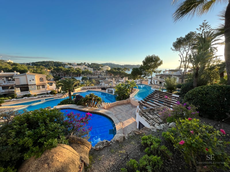 Multiple tiered blue swimming pools surrounded by lush tropical gardens and Mediterranean villas at sunset.