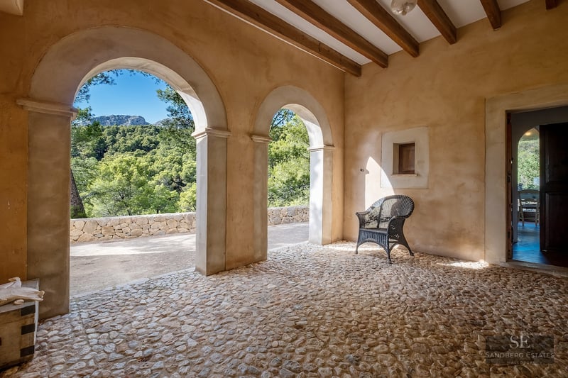 Rustic terrace featuring stone arches, wooden beams, cobblestone flooring, and a scenic mountain forest view.