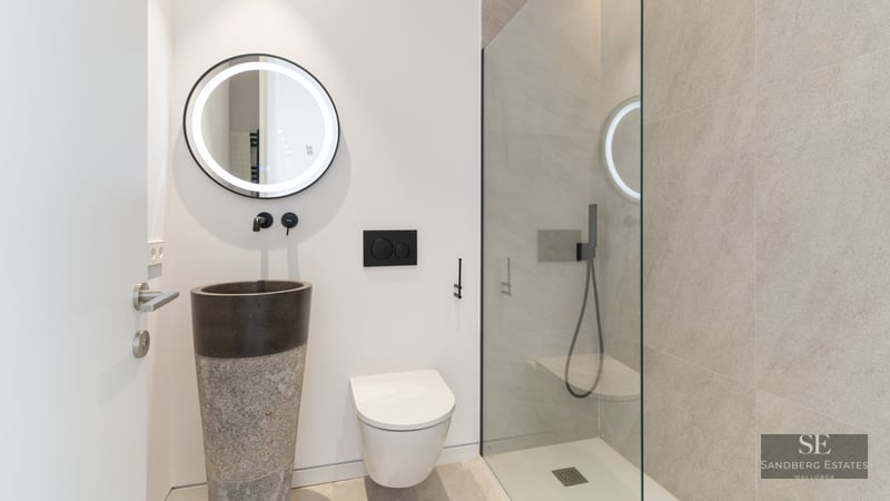 Contemporary bathroom featuring a unique stone pedestal sink, backlit round mirror, and a glass-enclosed walk-in shower.