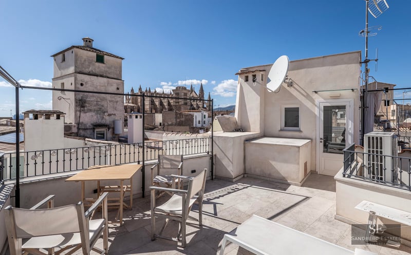 Toit-terrasse spacieux avec mobilier en bois et vue imprenable sur la cathédrale historique sous un ciel bleu.