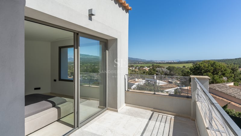 Privat terrass med naturstensgolv och skjutdörrar i glas med utsikt över en grönskande dal.