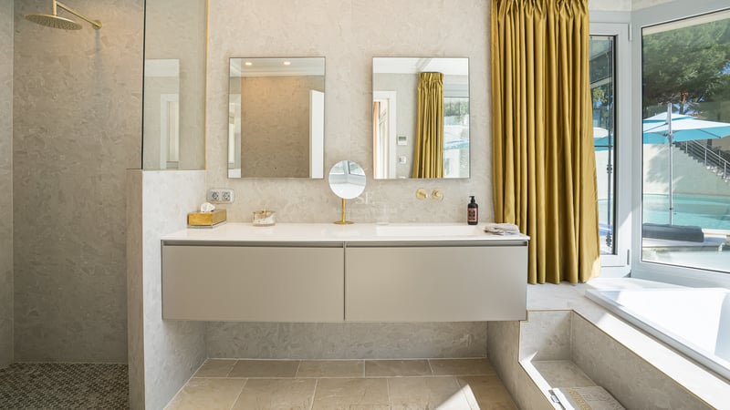 Modernes Badezimmer mit beigem schwebendem Doppelwaschtisch, zwei Spiegeln und goldfarbenen Vorhängen.