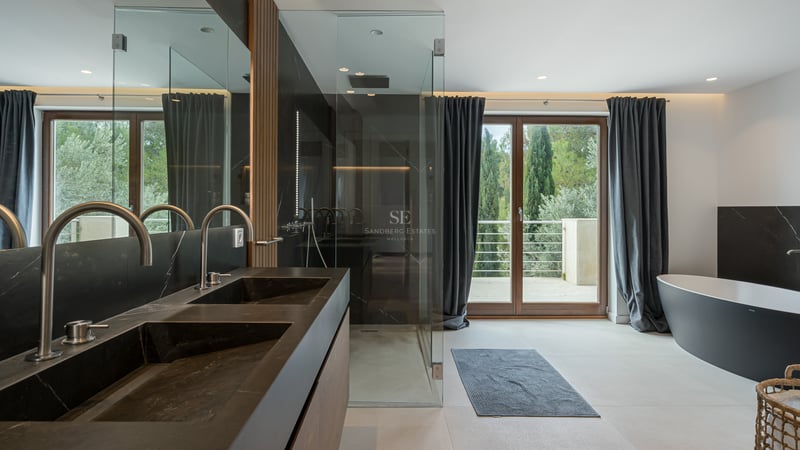 Salle de bains moderne avec double vasque noire, douche à l'italienne, baignoire îlot et vue sur la forêt.